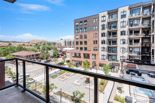 Balcony with glass railing overlooking apartment buildings, a landscaped courtyard and the street below.