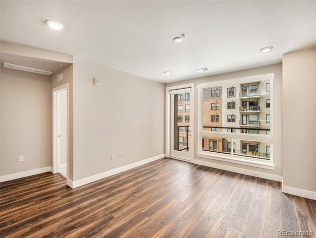 Empty room with wood flooring and large windows overlooking neighboring apartment buildings.