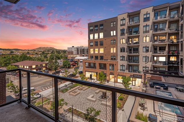 Balcony view over Denver apartment buildings and streets beneath a pink-orange sunset.