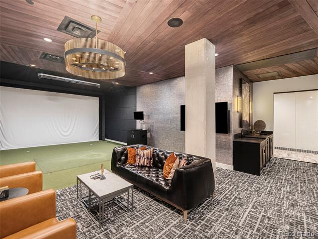 Furnished media room with a projection screen, leather sofa, orange armchairs, and wood-plank ceiling.