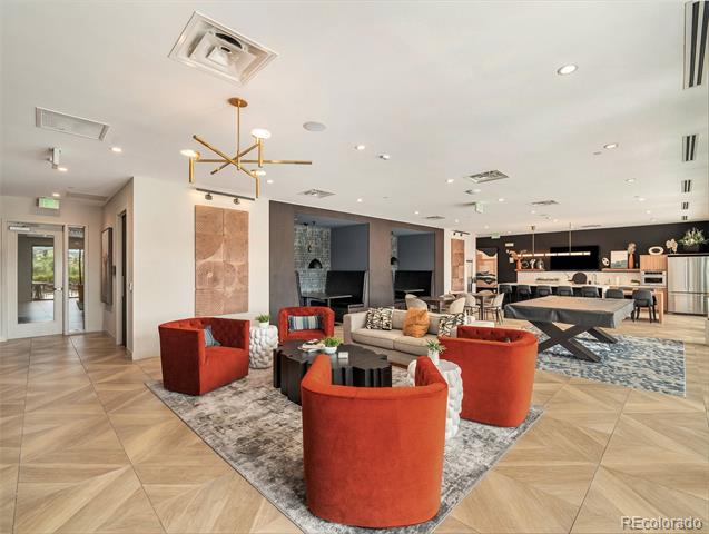 Furnished lounge with red chairs, patterned rugs, and a kitchen counter in the background.