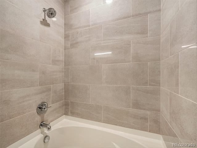 Bathroom tub with beige tile surround, chrome showerhead and faucet.