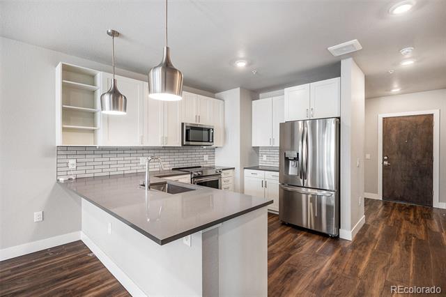 Modern kitchen with a large peninsula, stainless-steel appliances, and dark wood floors.