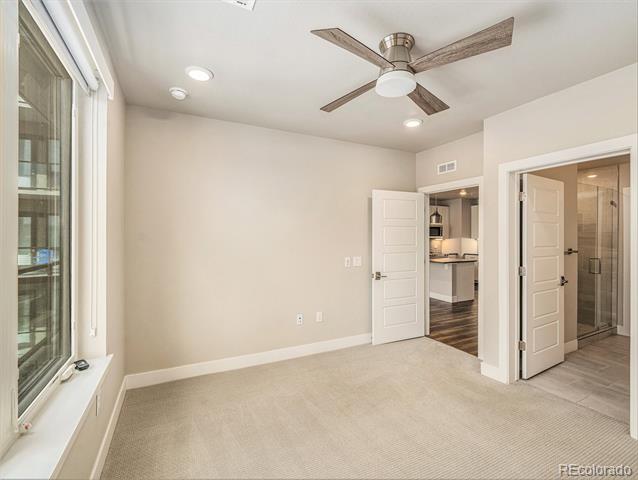 Vacant bedroom with a wood-blade ceiling fan, large windows, and doors to the kitchen and bathroom.
