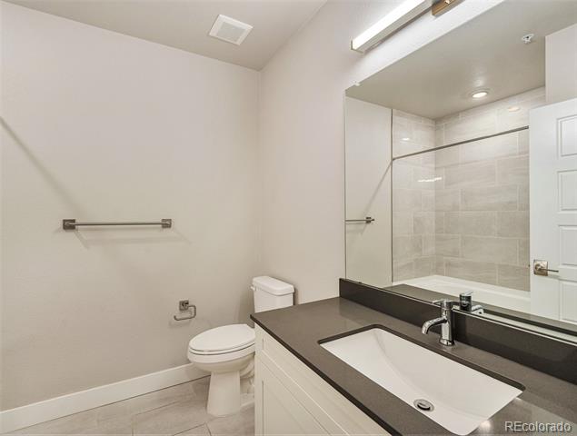 Bathroom with a dark vanity counter, white sink, large mirror, and tiled shower reflected behind it.