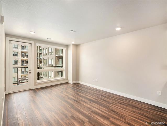 Unfurnished room with dark wood floors and large windows overlooking a neighboring building.