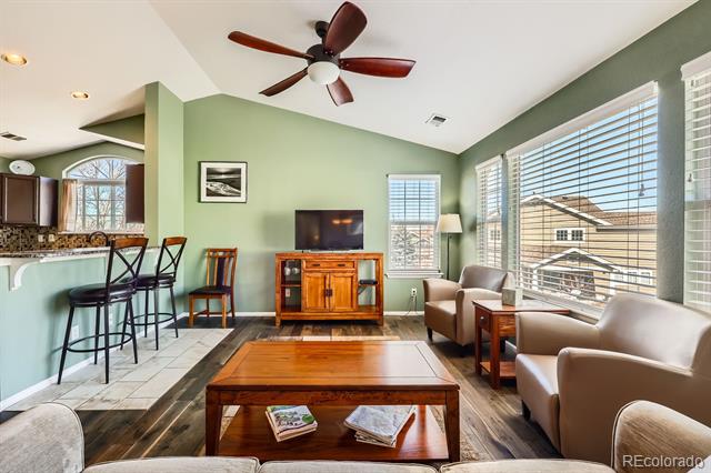 Living room with sage-green walls, wood furniture, beige armchairs, and an open kitchen.