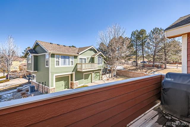 View from a wooden deck toward a green townhouse with balconies and garage doors.