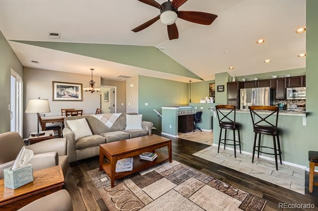 Open-plan living room with a gray sectional, patterned rug, and kitchen island with bar seating.