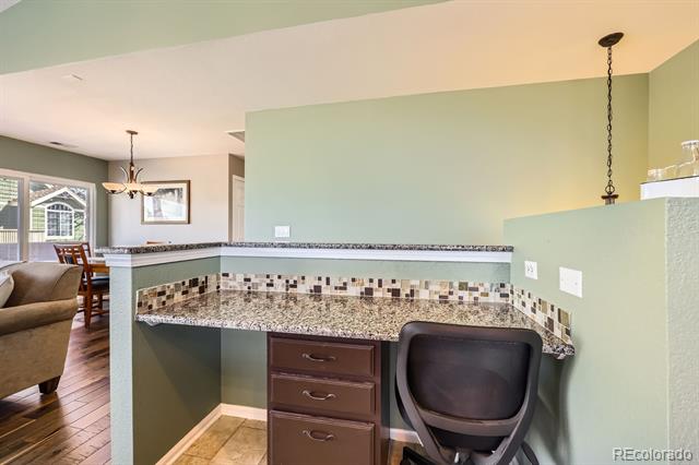 Kitchen workstation with granite counters, tiled backsplash, dark drawers, and a black office chair.