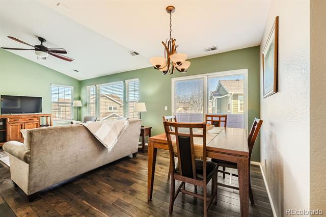 Open-plan living and dining room with sage-green walls, dark wood floors, and large windows.