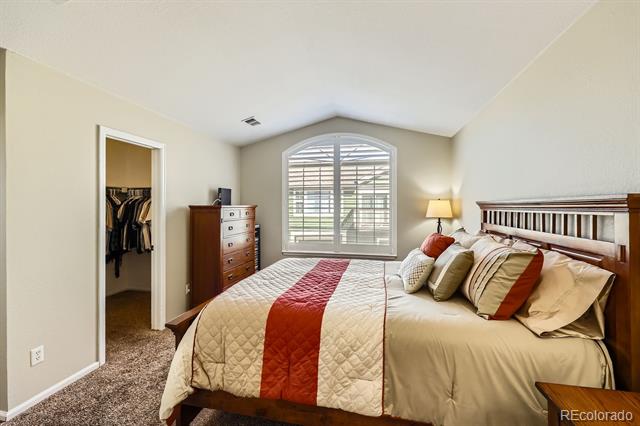 Bedroom with cream bedding, a rust-red runner, an arched shuttered window, and an open closet.