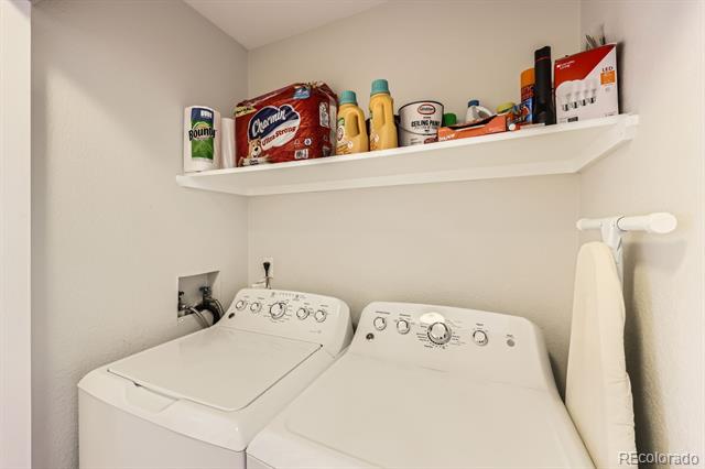 Laundry room with white washer and dryer, a stocked shelf, and a hanging ironing board.