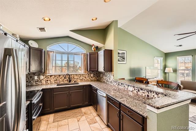 Kitchen with dark cabinets, granite counters, stainless appliances, and an arched window above the sink.
