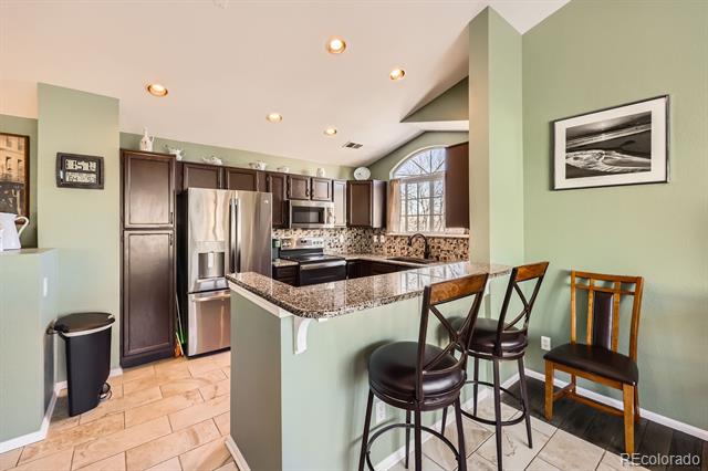 Kitchen with dark wood cabinets, stainless steel appliances, and a granite island with bar stools.