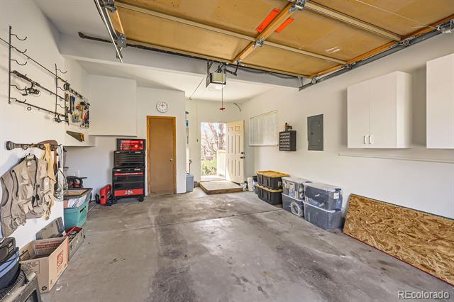 Garage with raised overhead door, concrete floor, wall cabinets, tools, and storage bins.