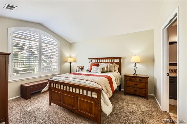 Bedroom with a wooden bed, rust-accented cream bedding, and a large arched shuttered window.