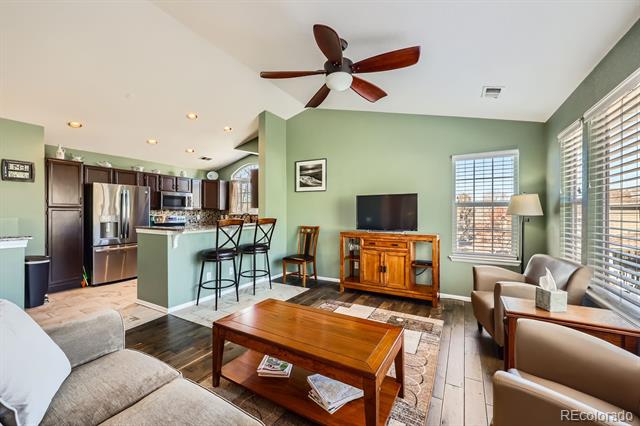 Living room with a wooden TV console and coffee table, opening onto a kitchen with a breakfast bar.