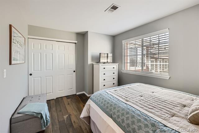 Furnished bedroom with a blue patterned bedspread, white dresser, and large window with blinds.