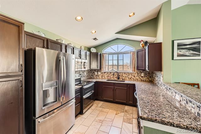 Kitchen with dark wood cabinets, stainless steel appliances, granite counters, and an arched window above the sink.