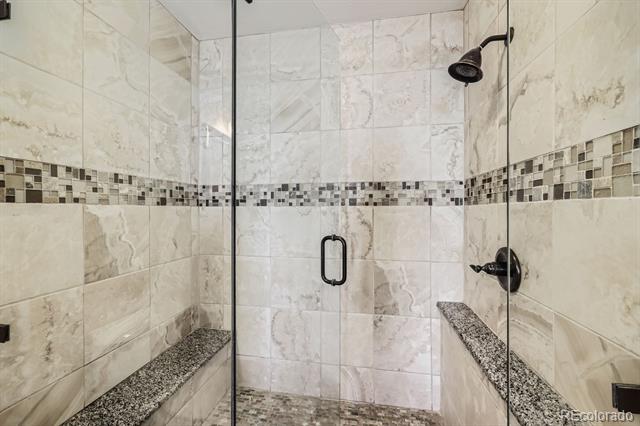 Walk-in shower with frameless glass, marble-look tile, mosaic accent band, and built-in granite-topped benches.