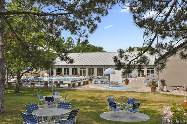 Community pool and outdoor seating beneath mature trees beside a low building.