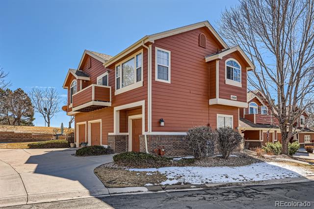 Two-story red-brown attached home with a small balcony and snow patches on the lawn.
