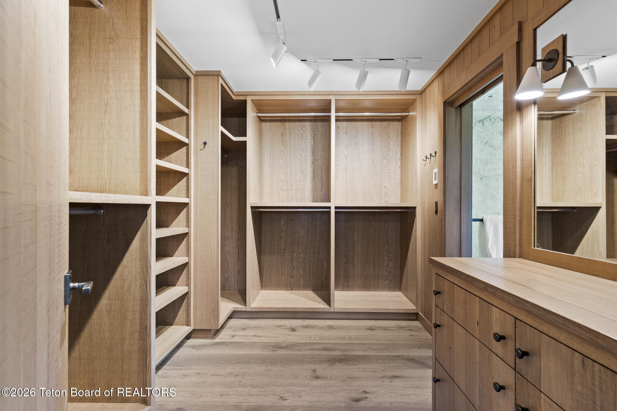 Walk-in closet with light wood built-ins, open shelving, hanging sections, and a long drawer counter.