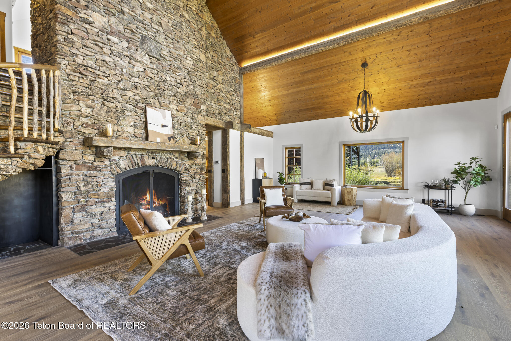 Living room with a soaring wood ceiling, stone fireplace, and curved white sofa.