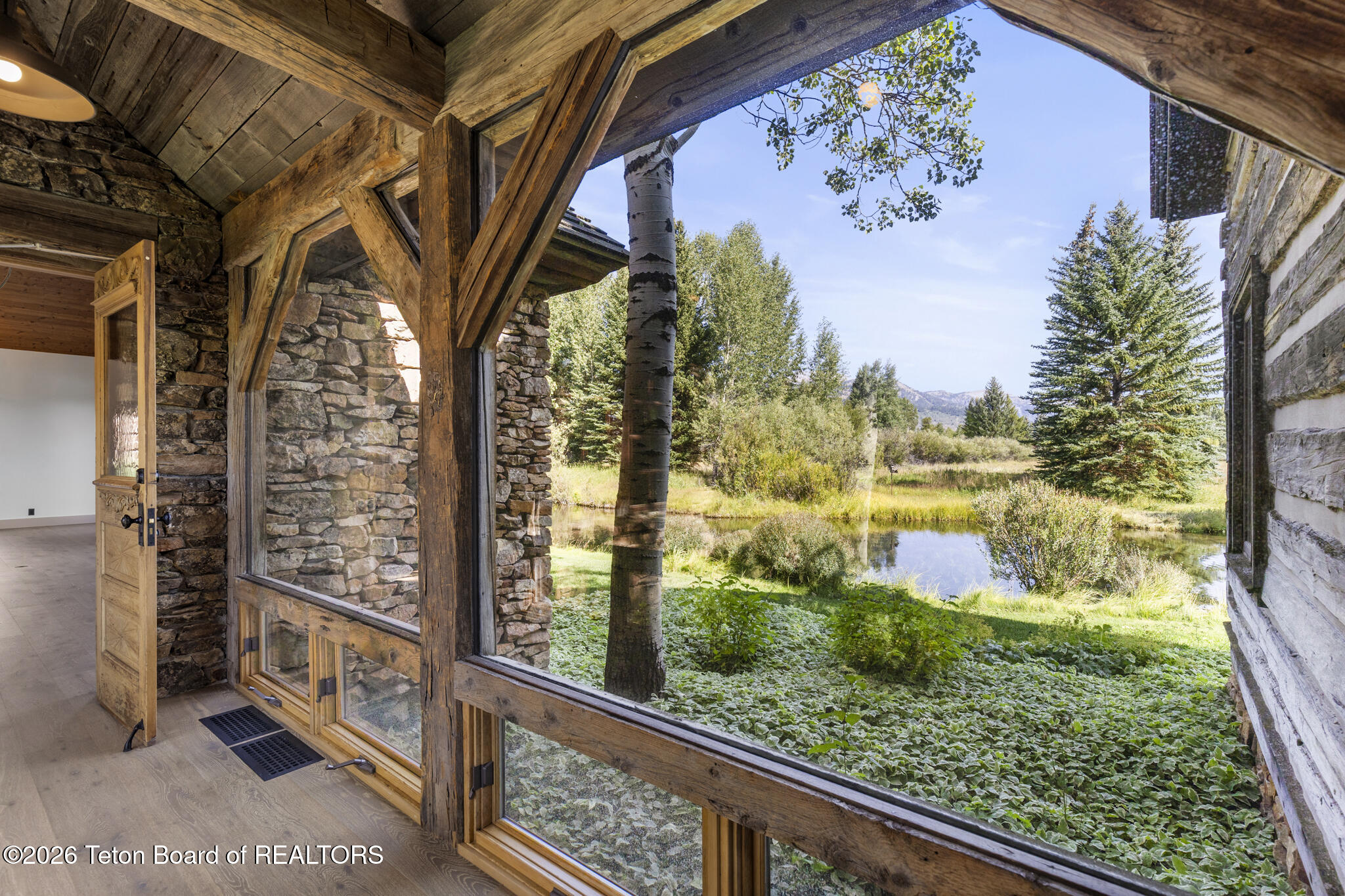Stone-and-timber interior framing a pond, evergreens, and distant mountain view.