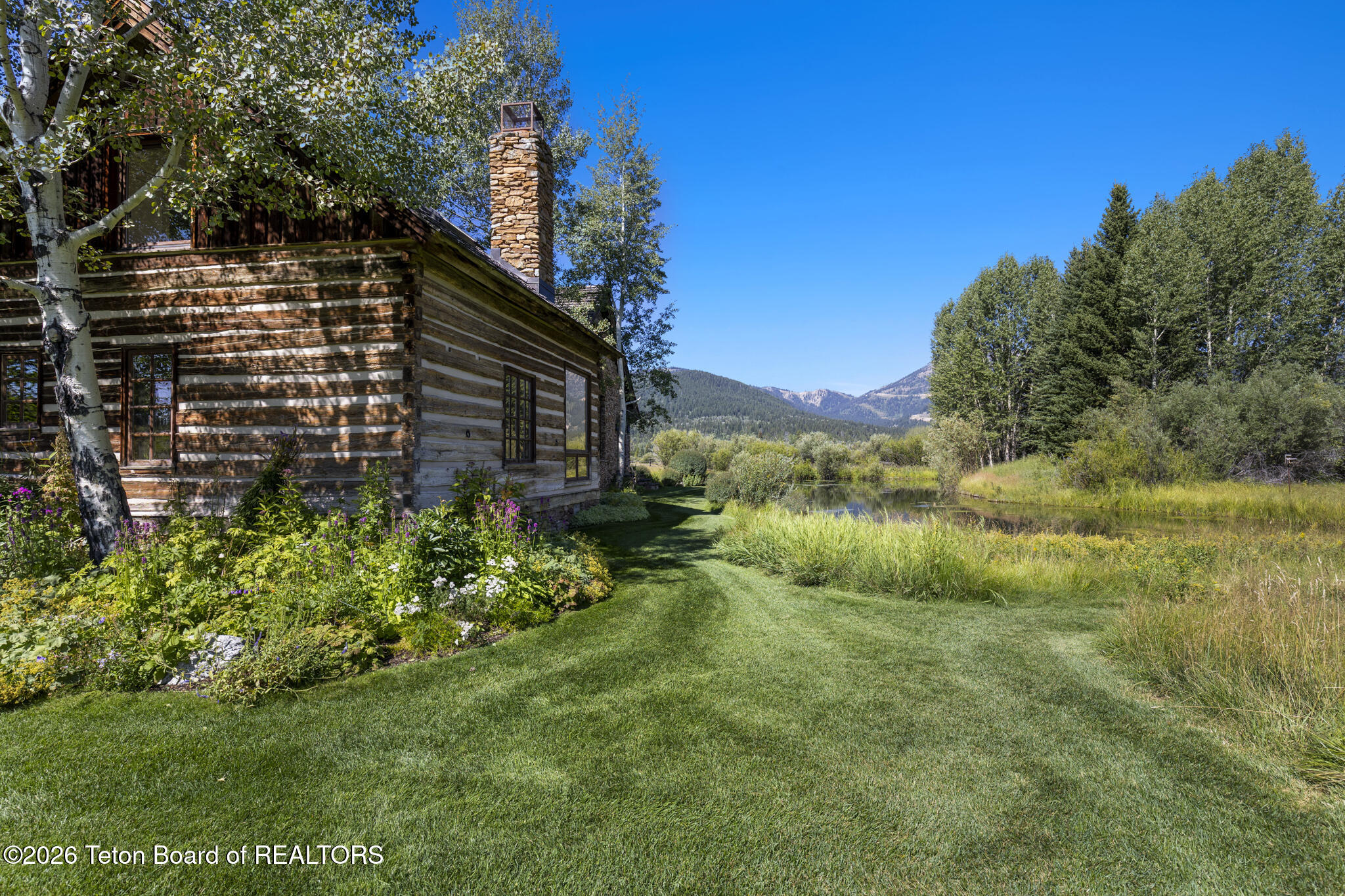 Rustic log-sided home beside a pond, with flowering gardens and mountain views.