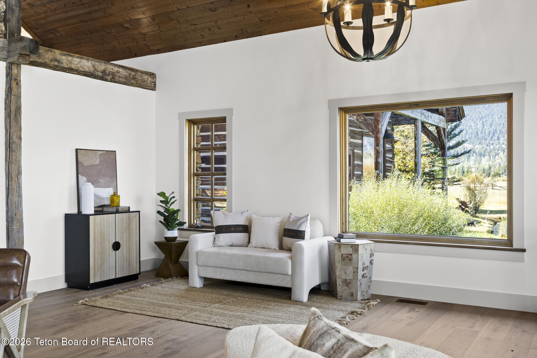 Living room with a white sofa, exposed timber beams, and mountain views through large windows.