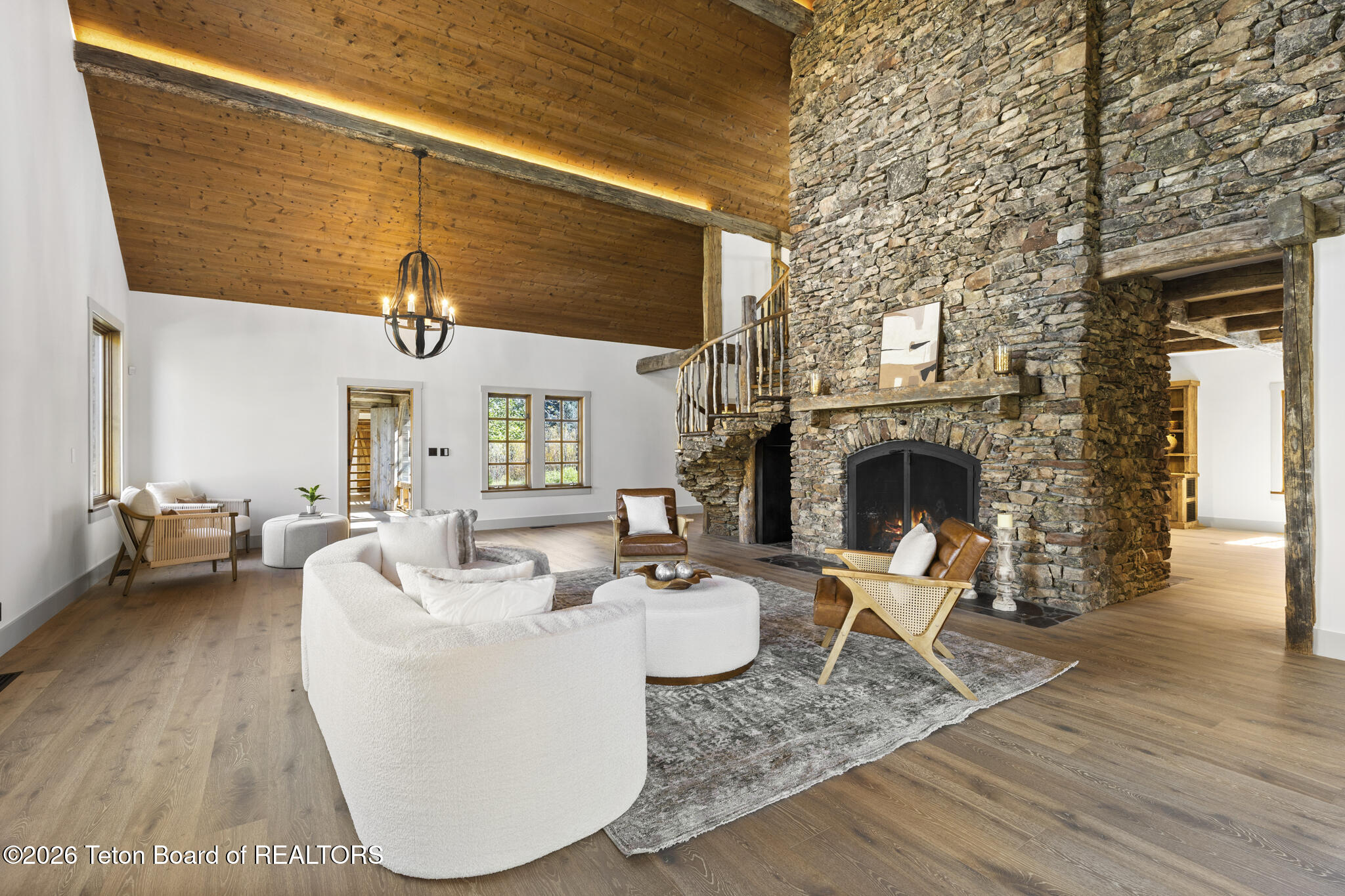 Staged living room with a towering stone fireplace and vaulted wood ceiling.