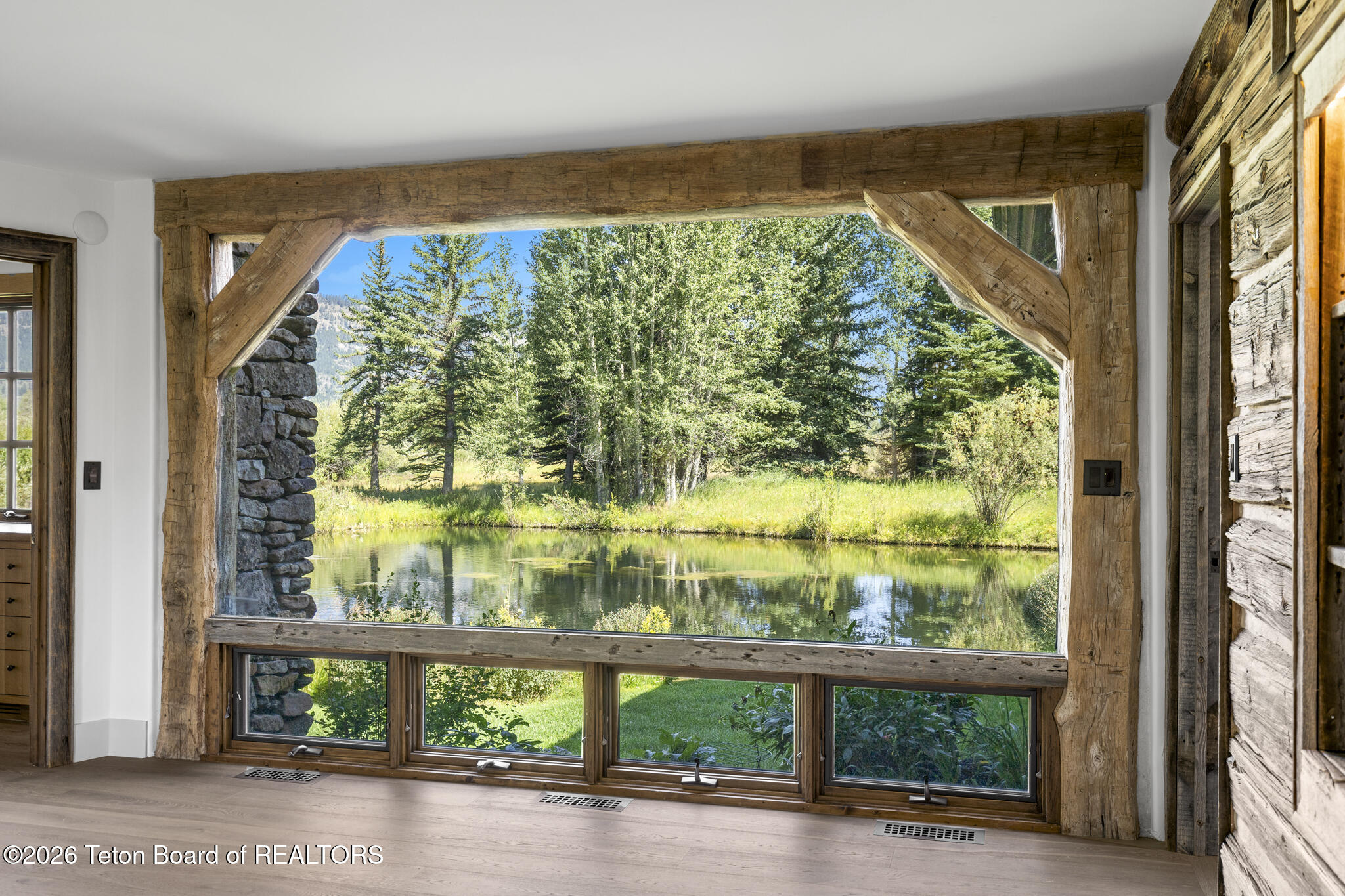 Empty timber-framed room with a large window overlooking a pond and trees.