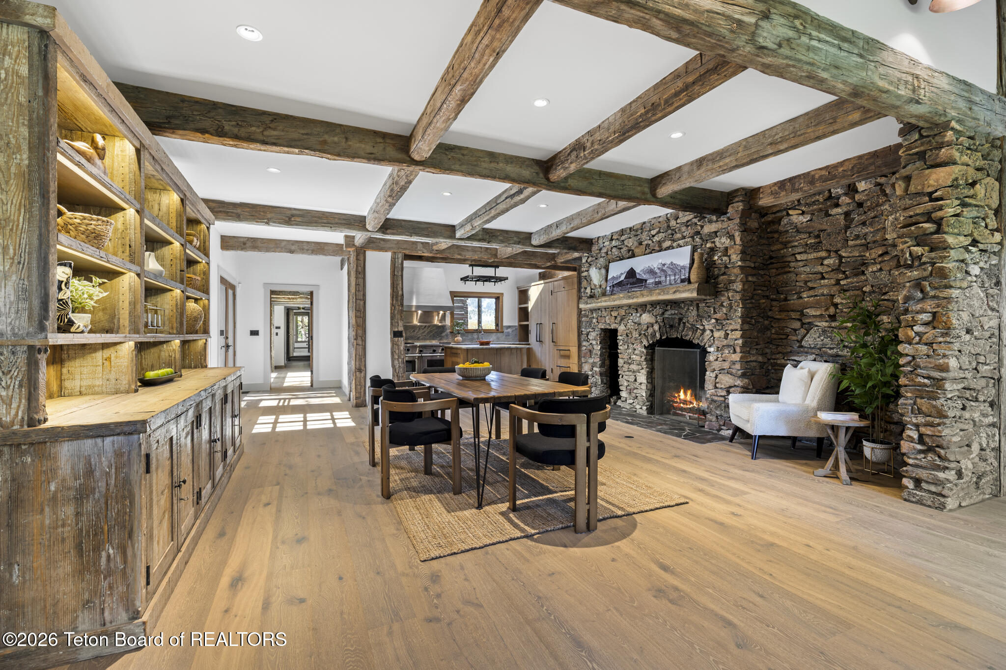 Open dining and living area with exposed timber beams and a large stone fireplace.