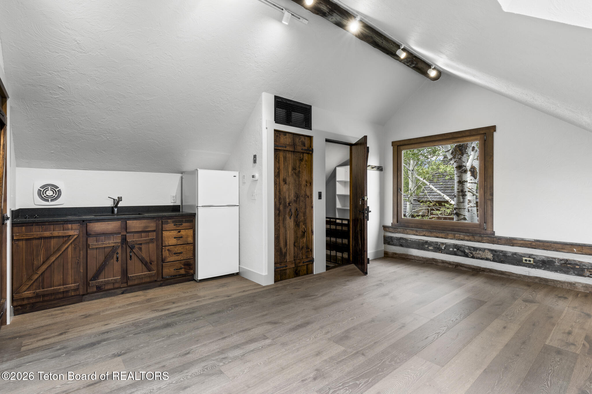 Compact kitchenette with rustic wood cabinets, a white refrigerator, and an aspen-framed window.