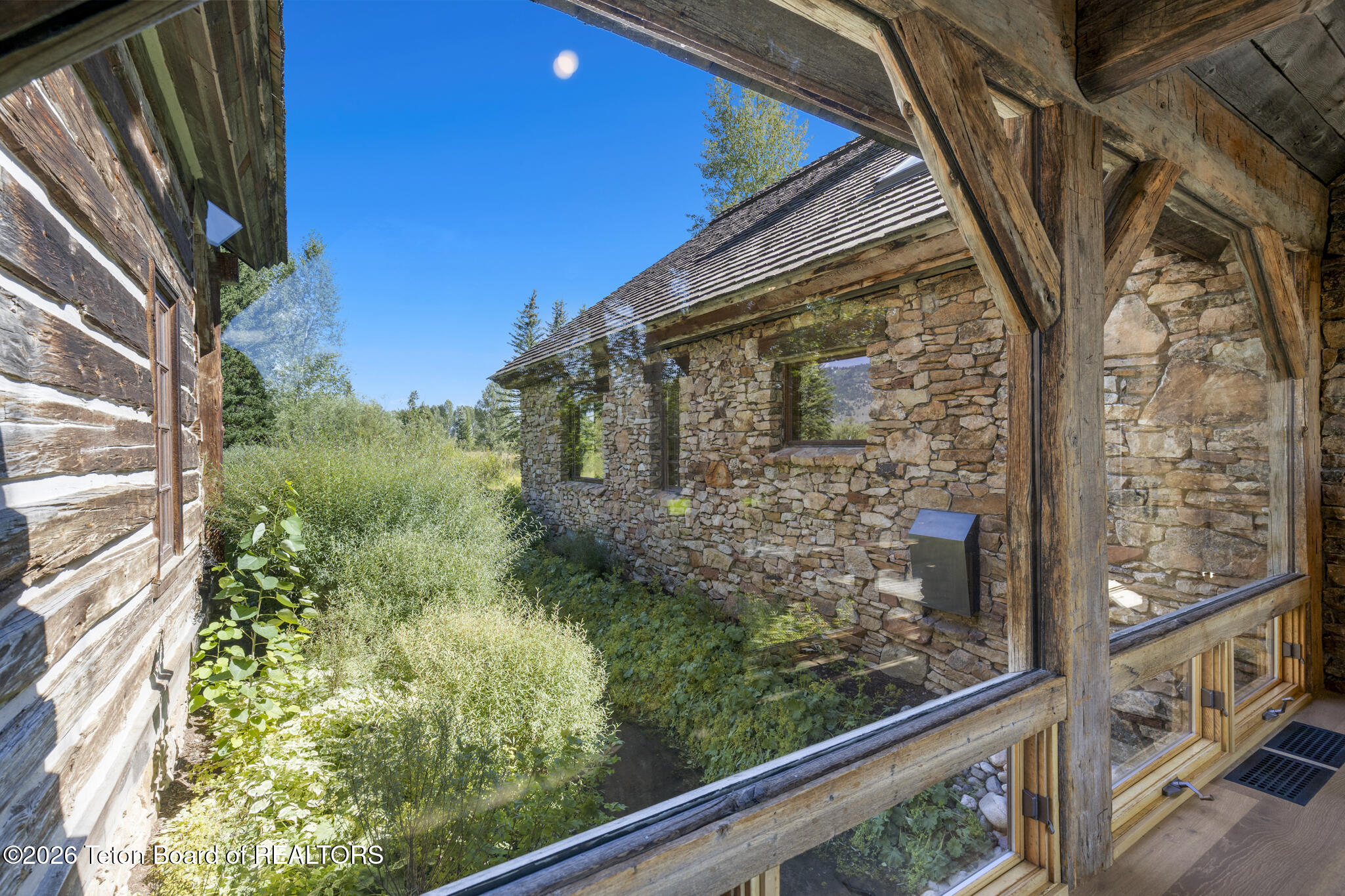 Rustic stone-and-timber courtyard with large windows and leafy landscaping.