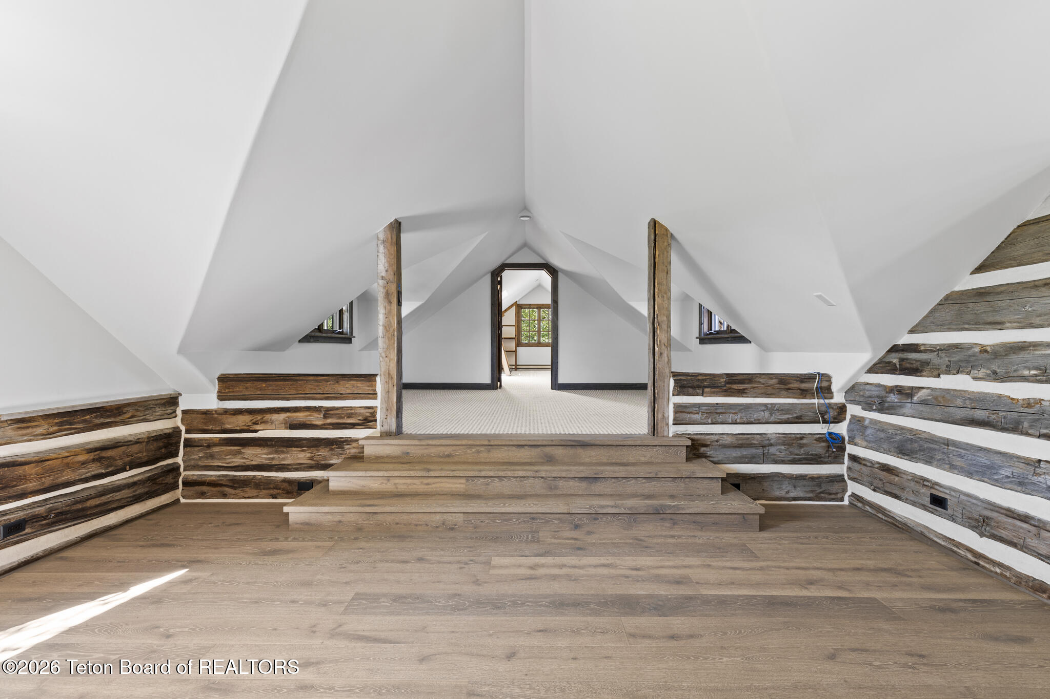 Attic interior with a vaulted ceiling, rustic log walls, and steps leading to a raised doorway.