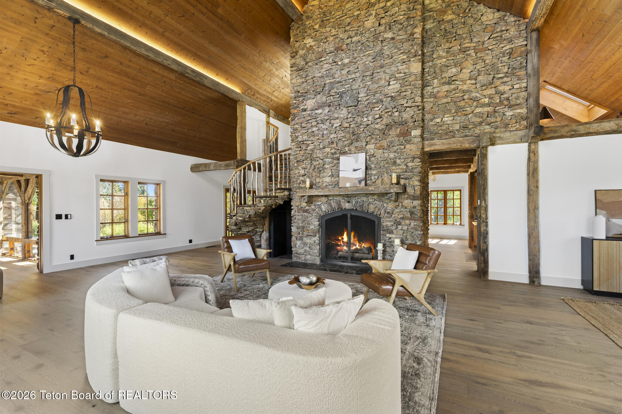 Living room with a towering stone fireplace, vaulted wood ceiling, and curved staircase.