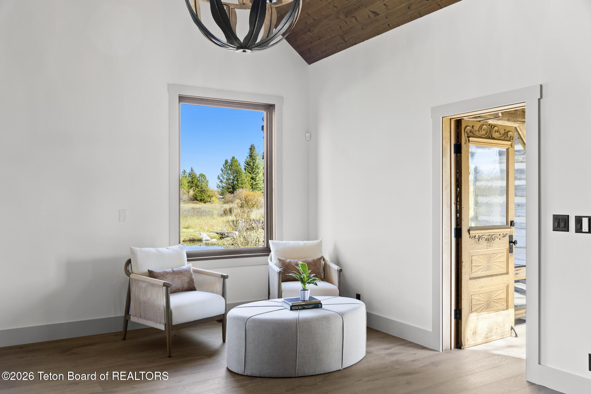 Furnished sitting area with a vaulted wood ceiling, nature views, and an open carved wooden door.