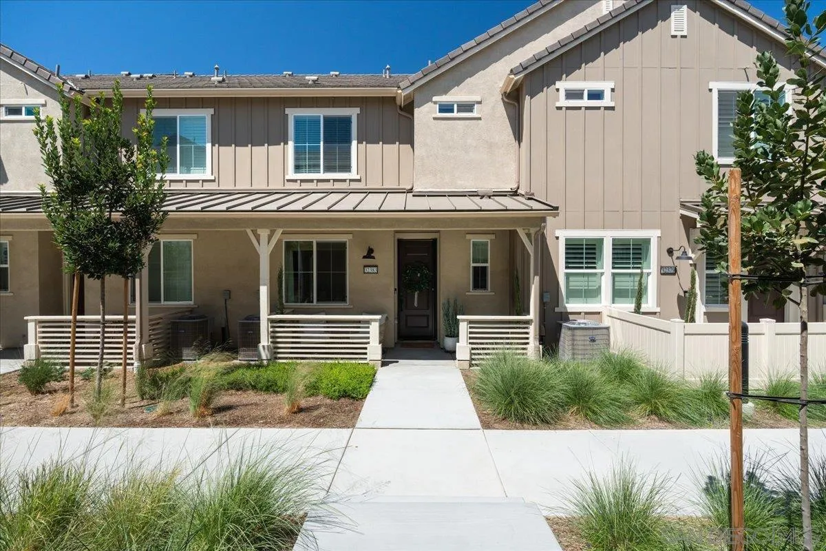 Two-story beige townhouse with a covered porch and landscaped walkway to the front door.
