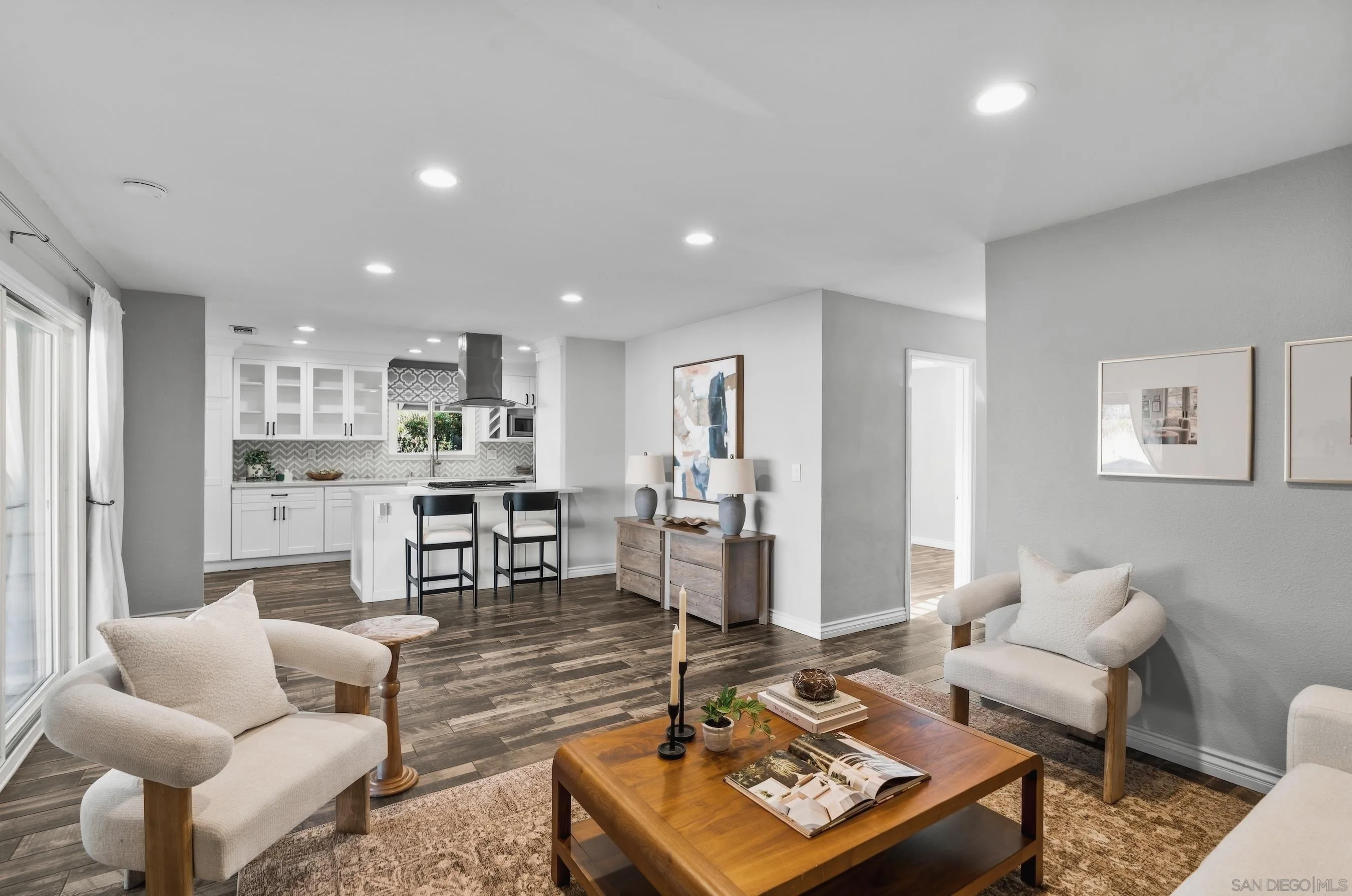 Open-plan living room and kitchen with cream chairs, a wood coffee table, and white cabinetry.