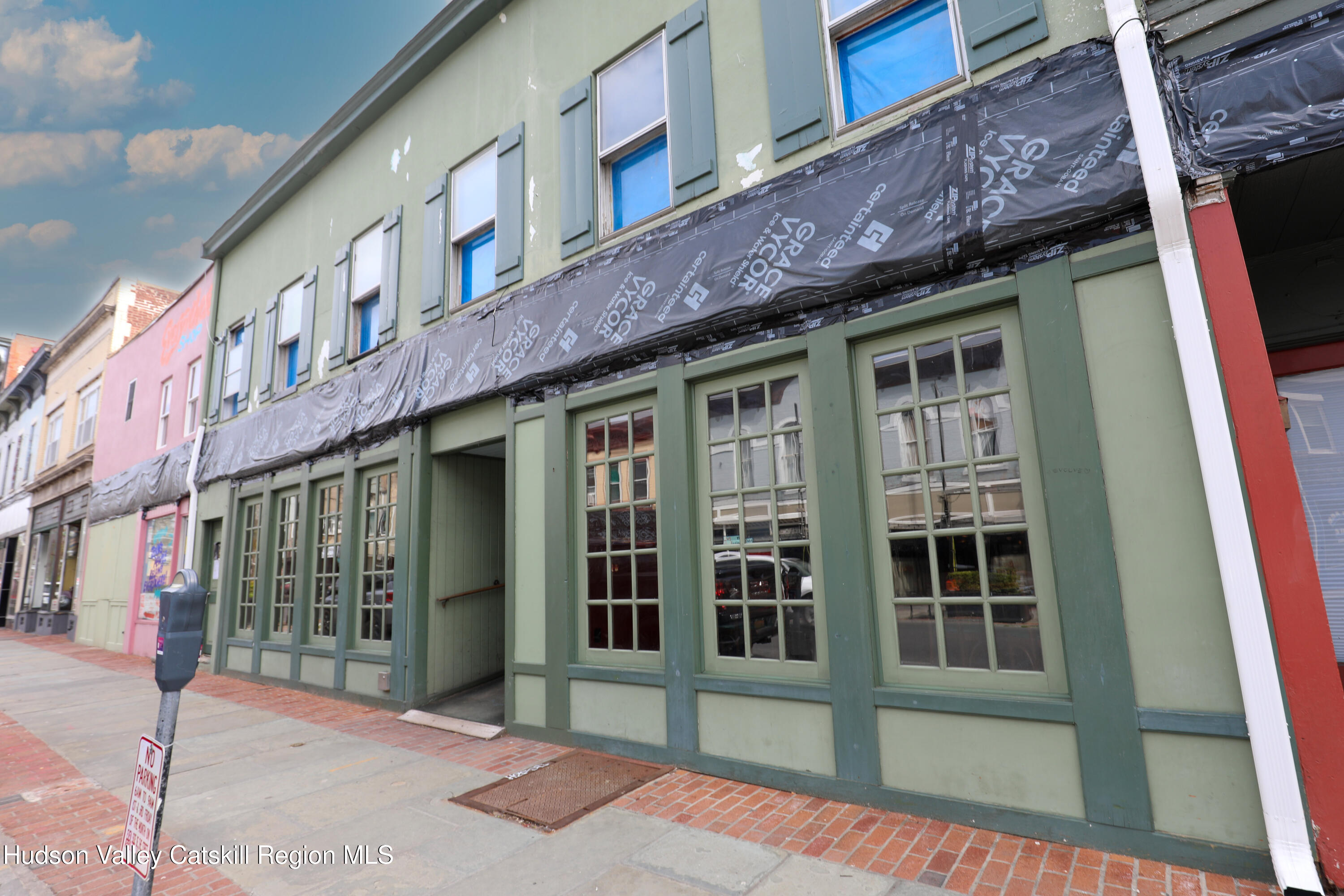 Green commercial building with large storefront windows and renovation wrap across its upper facade.