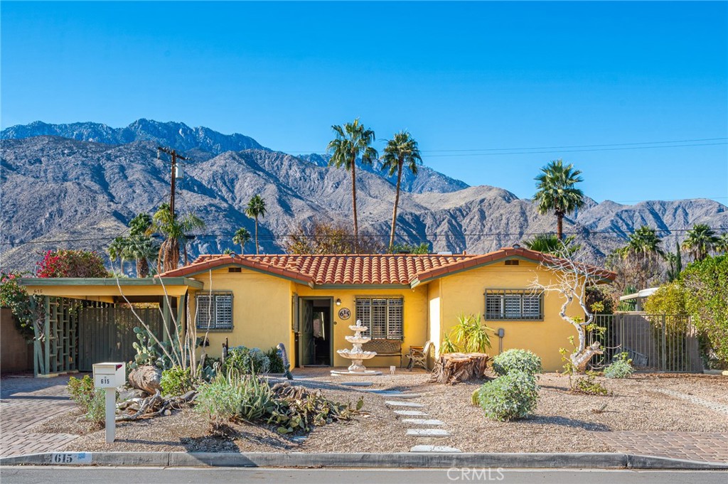 Yellow single-story home with a red tile roof, desert landscaping, and mountains behind it.