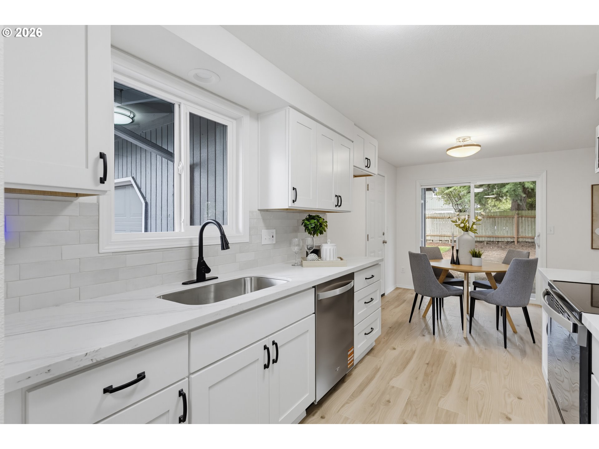 Bright white kitchen with black fixtures and a dining nook beside sliding glass doors to a fenced yard.