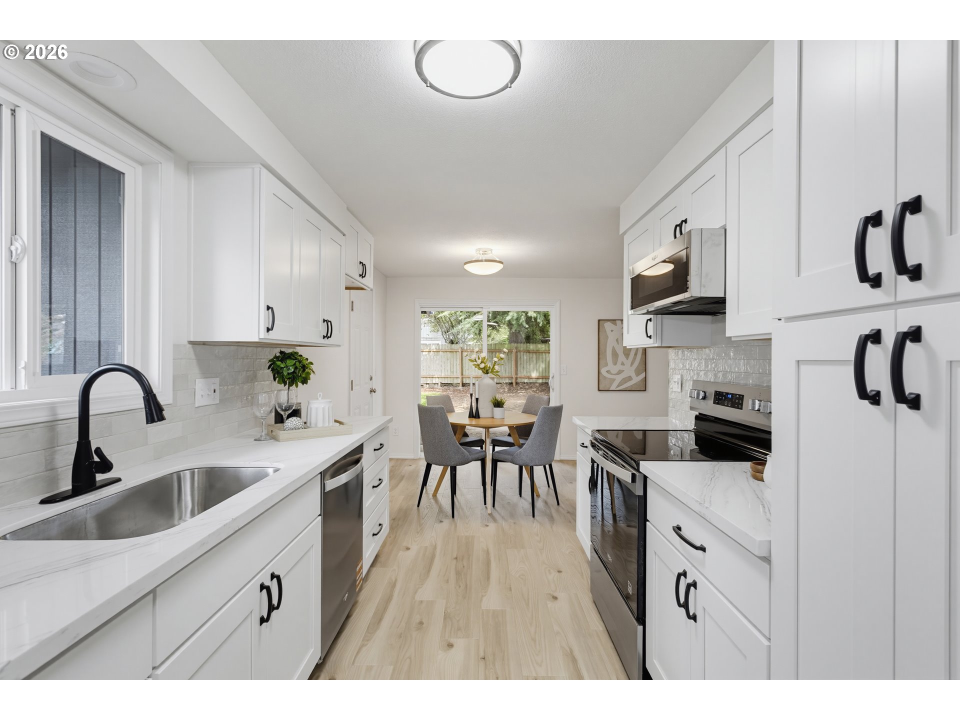 Bright white kitchen with marble-look counters, stainless steel appliances, and a dining table by the window.