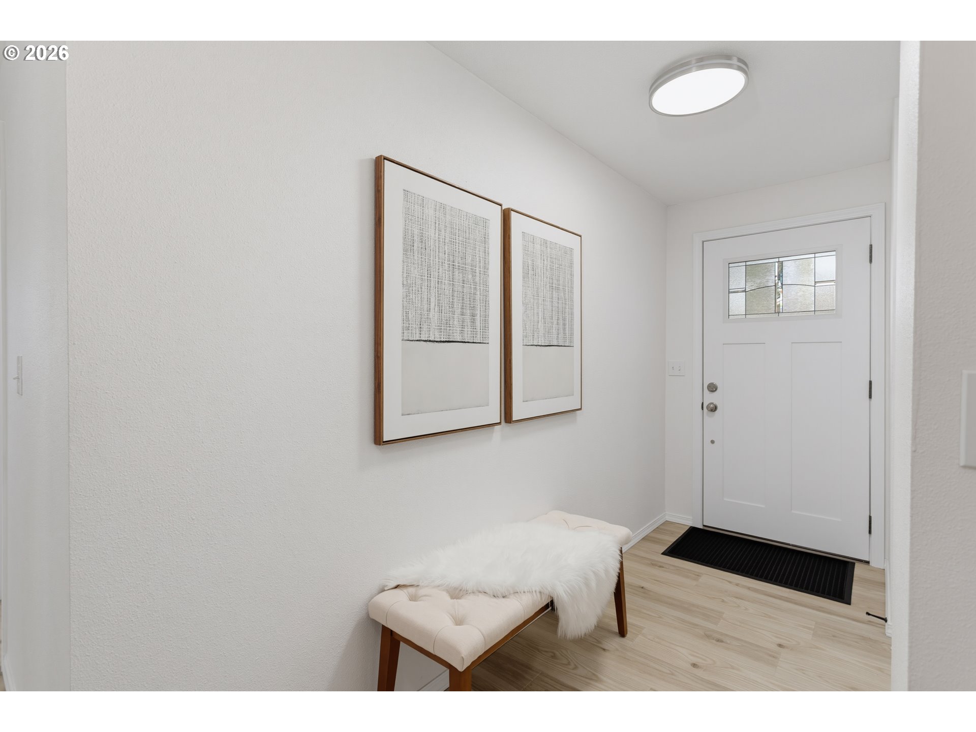 Bright entryway with a glass-panel front door, framed art, and a cushioned bench.