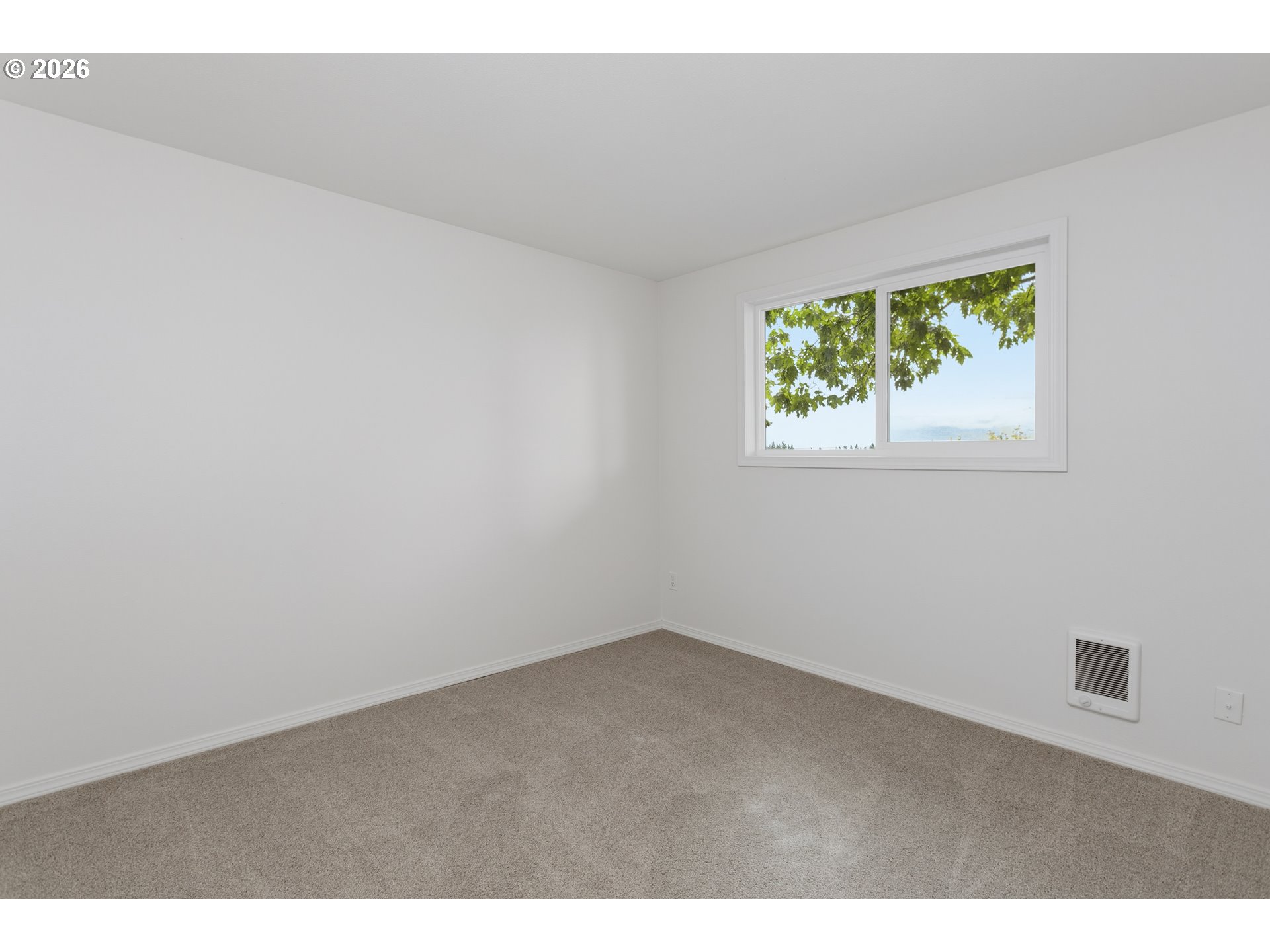 Empty carpeted room with white walls, a small window, and a wall heater.