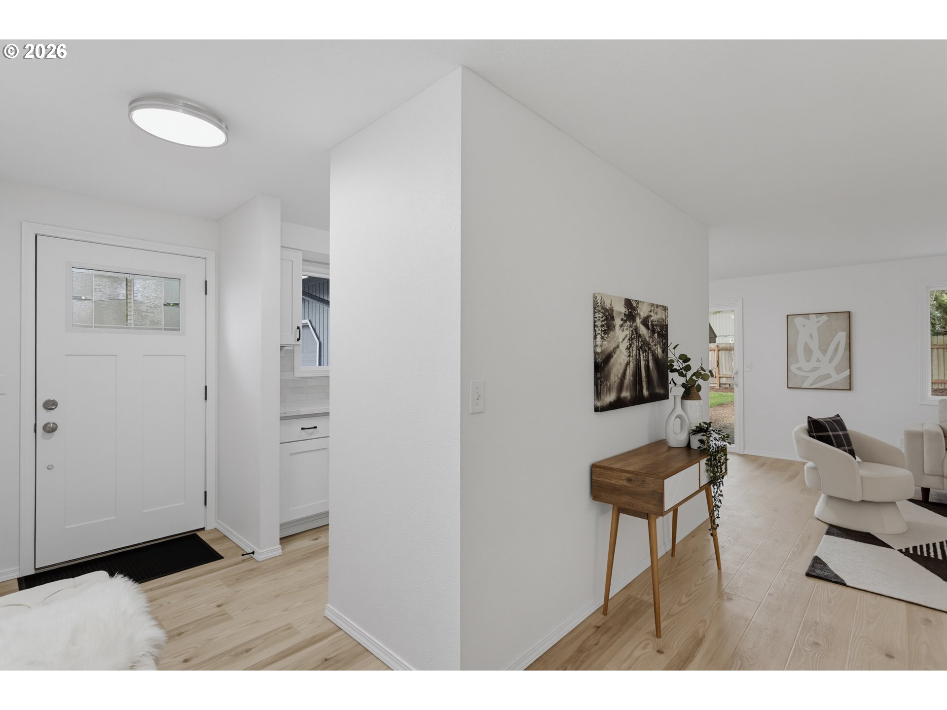 Bright entryway opening into a living area with light wood floors and a white lounge chair.