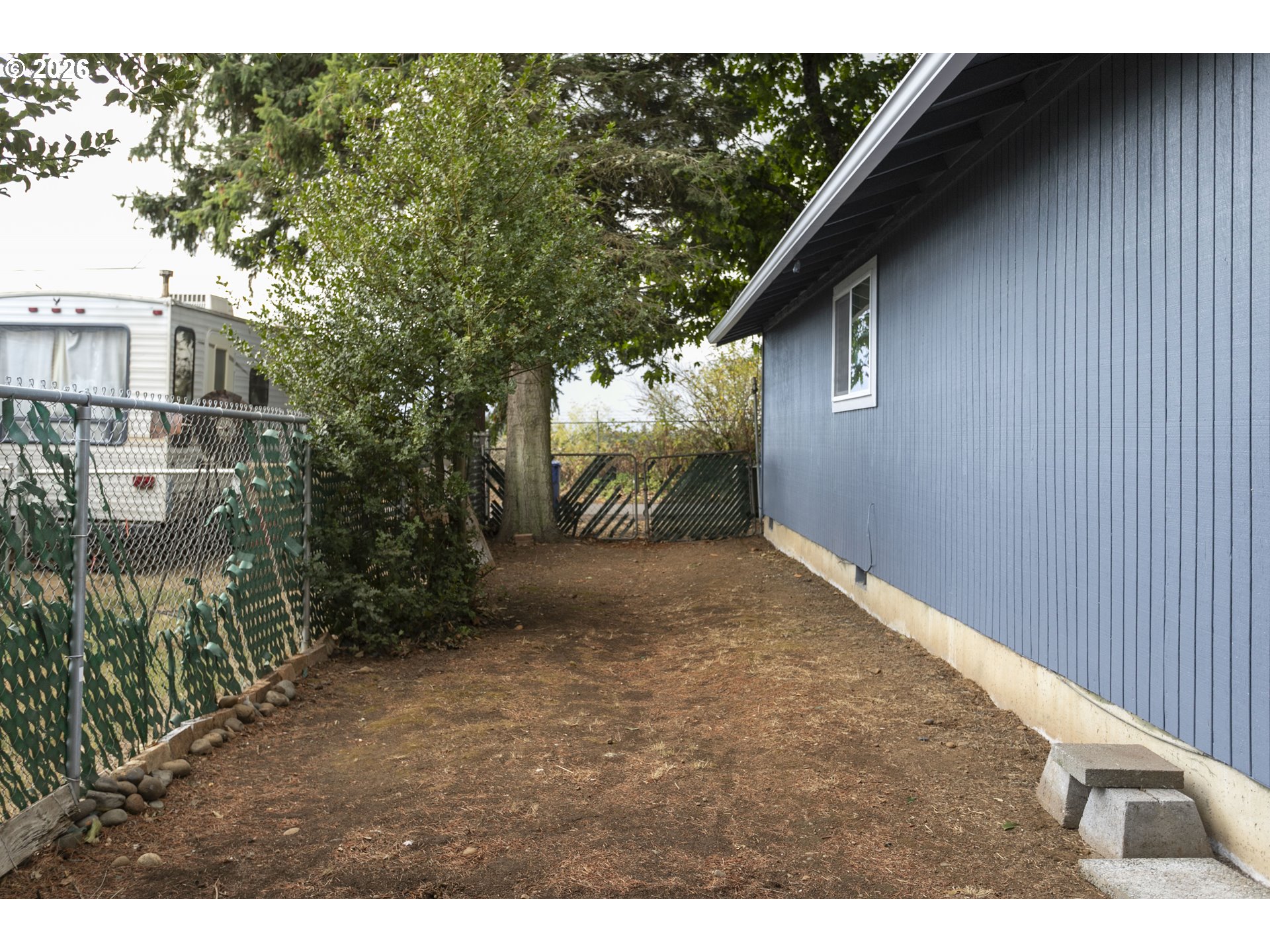 Side yard beside a blue house, with a chain-link fence and rear gate.